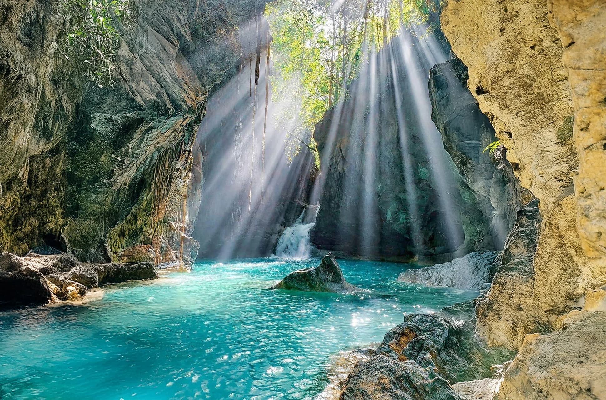 Sunlight streaming through jungle cliffs onto a hidden waterfall at Río Partido, Dominican Republic.