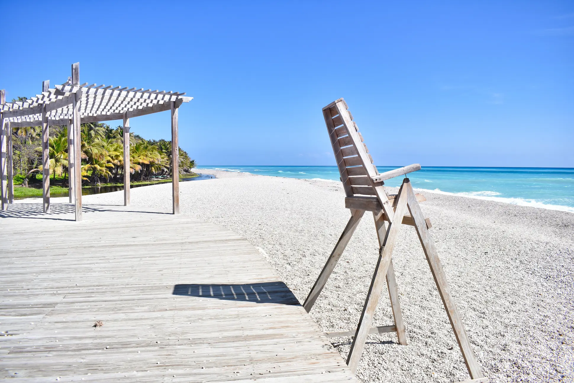 Scenic view of Los Patos Beach in Pedernales, Dominican Republic, showing turquoise waters, white pebbles, and wooden lifeguard chair.