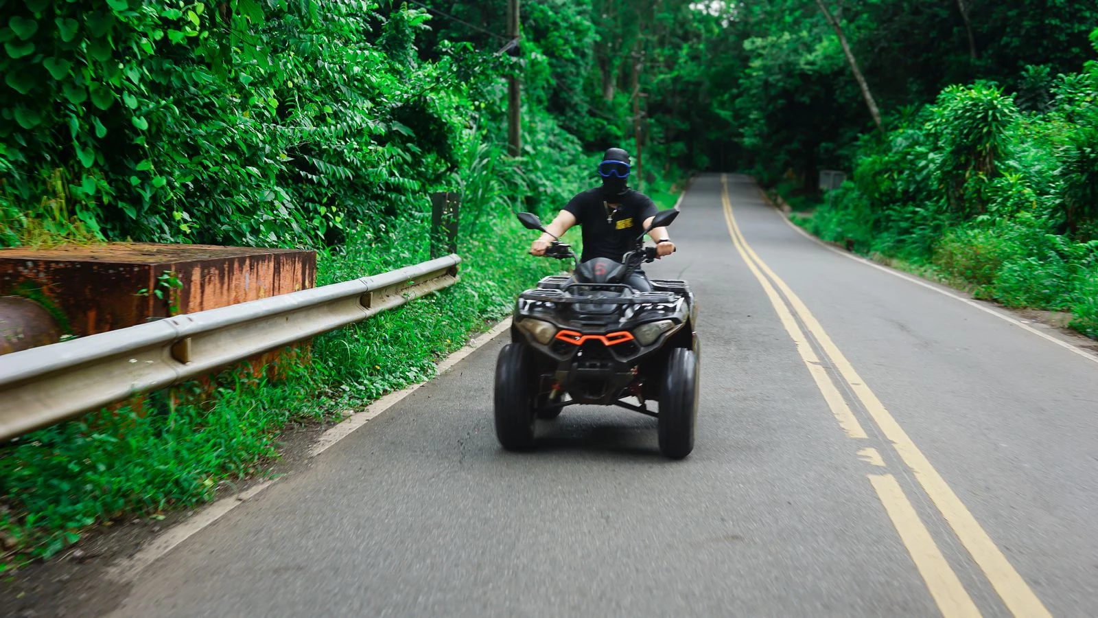 Rider driving ATV on scenic paved road surrounded by lush greenery in Comatillo, Dominican Republic