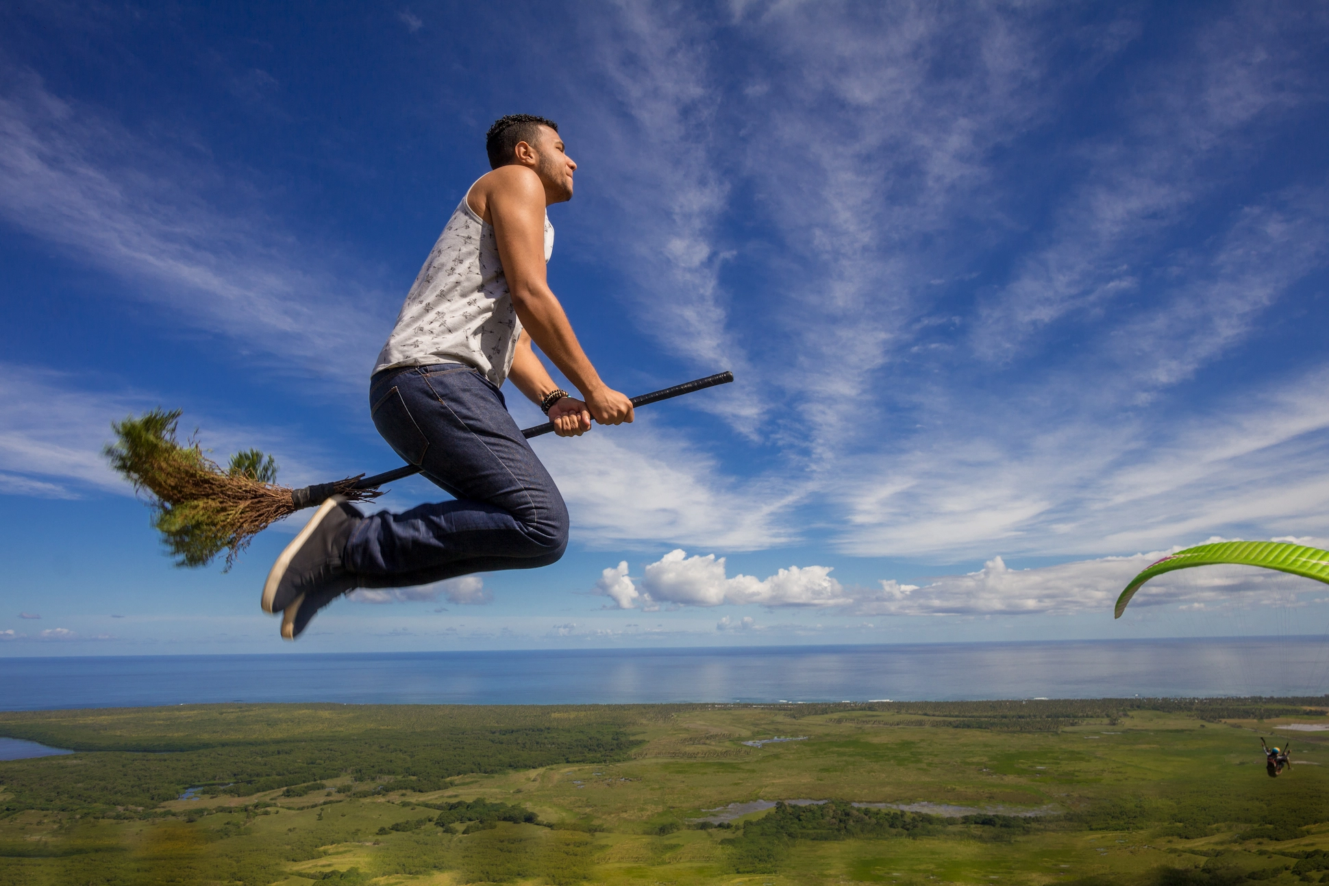 Man posing on a flying broom photo spot at Montaña Redonda with ocean view behind.