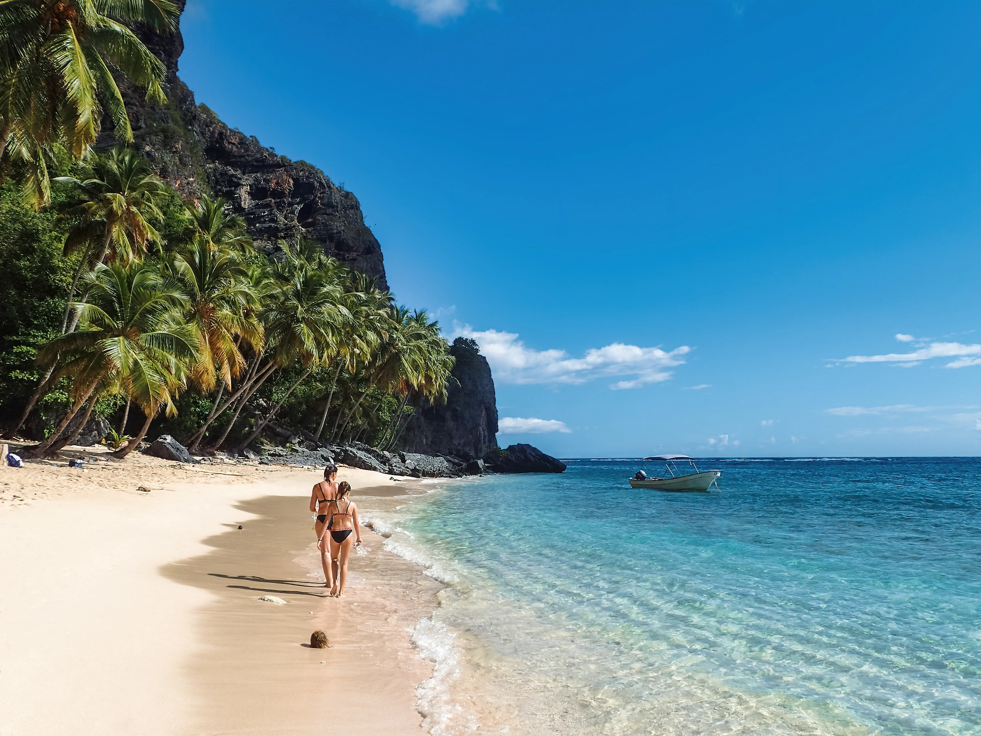 Couple walking along Frontón Beach with turquoise waters, palm trees and boat – tour from Santo Domingo