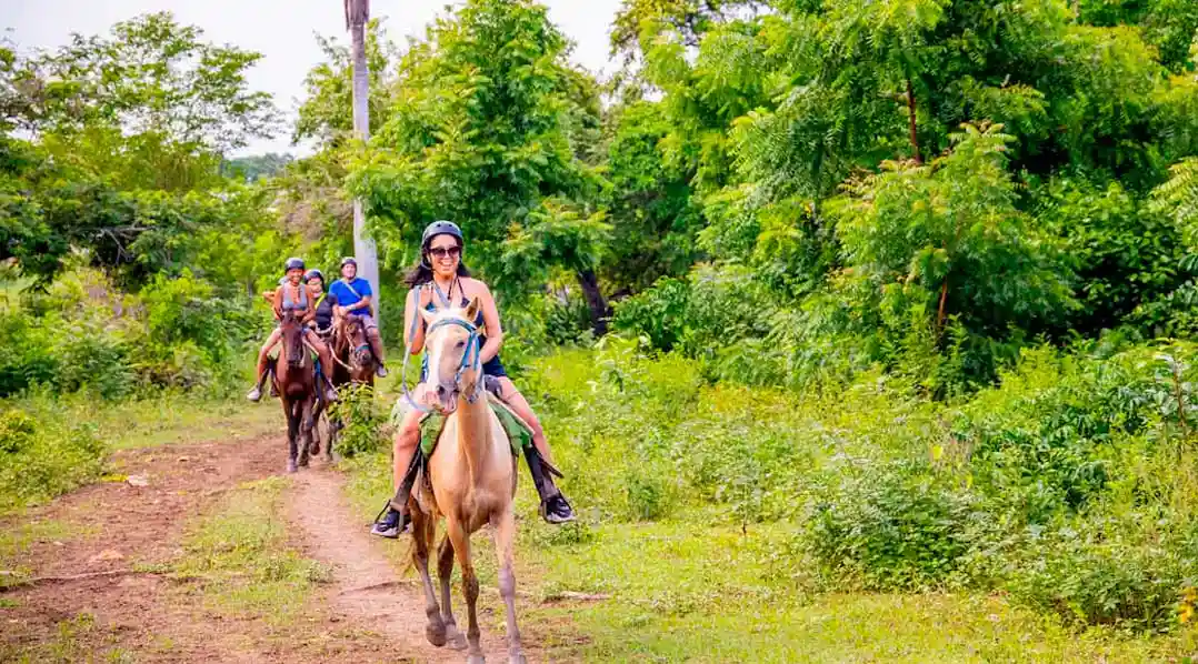 Travelers enjoying horseback riding through a green countryside trail in the Dominican Republic.