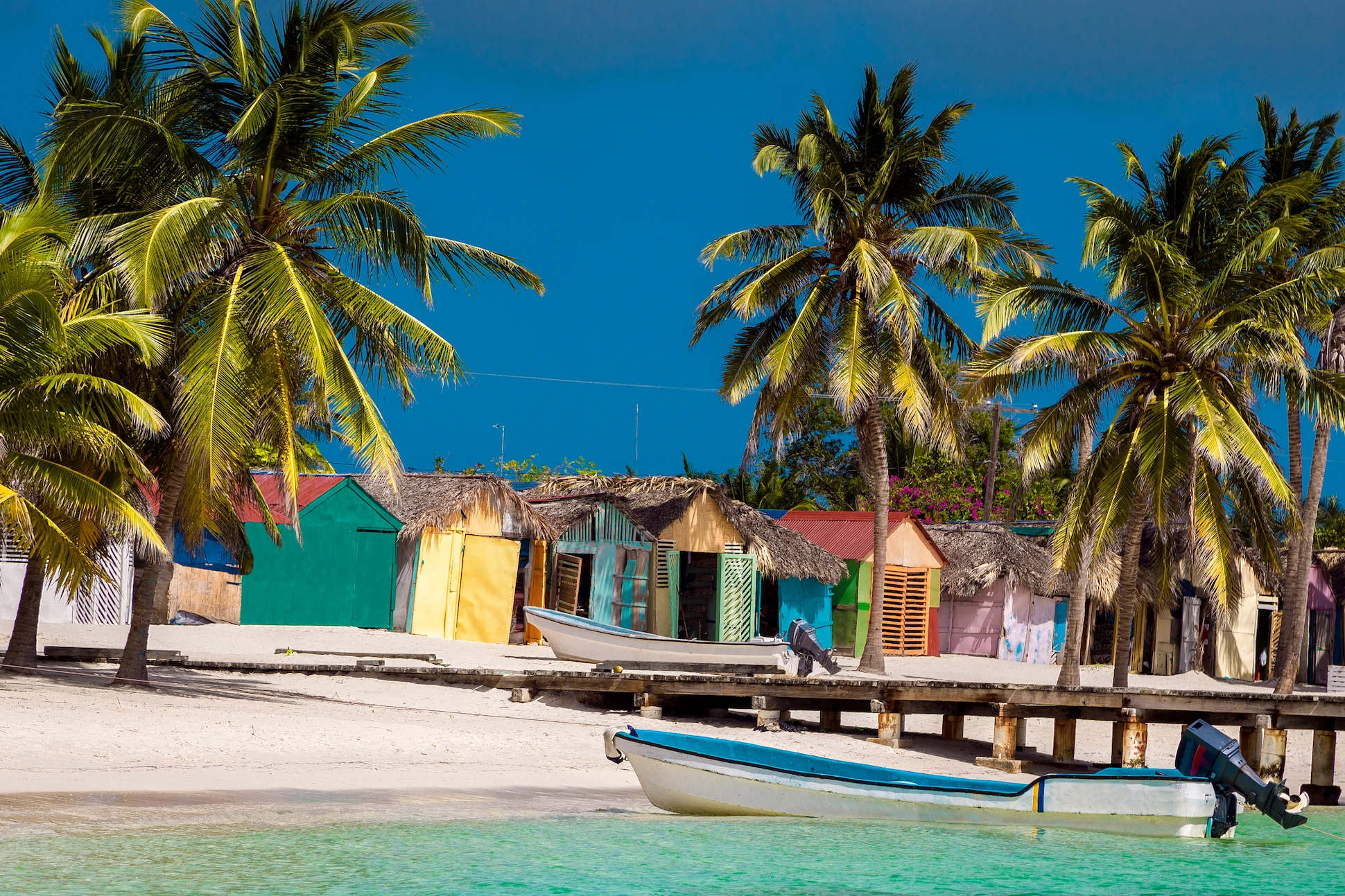 Colorful houses in Mano Juan Saona Dominican Republic with palm trees and fishing boats by the beach.