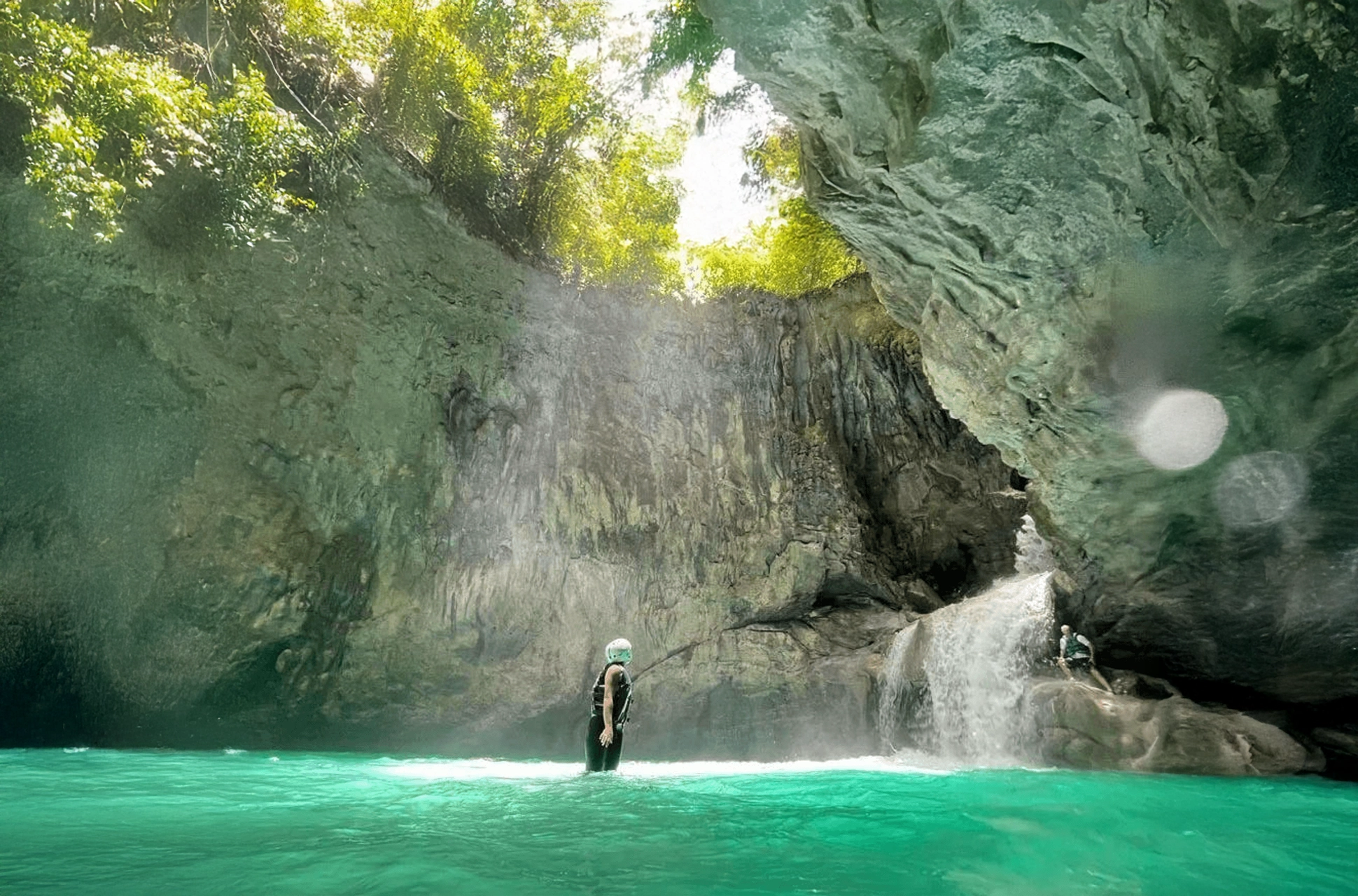 Explorer standing under a cave waterfall at Río Partido Hidden River in the Dominican Republic.