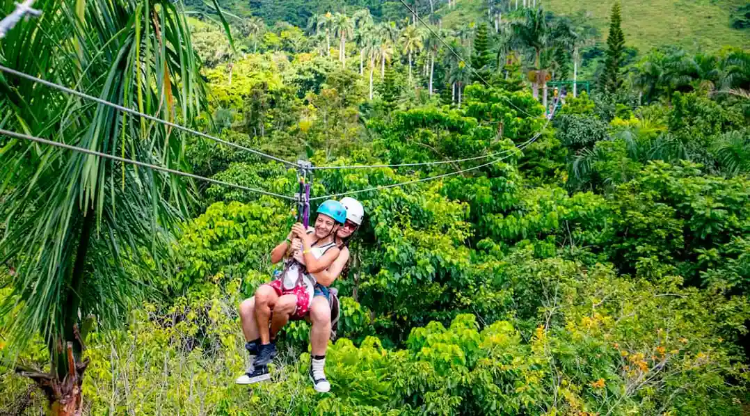 Two travelers enjoying a tandem zipline ride over the lush tropical forest in the Dominican Republic.