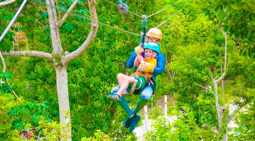 Parent and child enjoying a tandem zipline ride over lush green forest in the Dominican Republic.